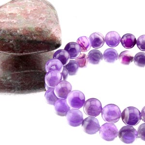 May include: A purple amethyst gemstone bracelet with round beads. The bracelet is made of natural amethyst stones and is a beautiful example of this popular gemstone.