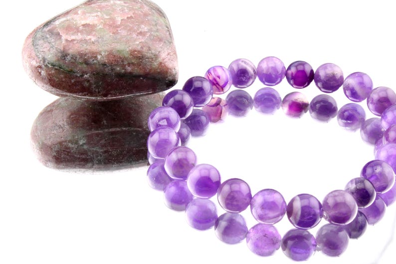 May include: A purple amethyst gemstone bracelet with round beads. The bracelet is made of natural amethyst stones and is a beautiful example of this popular gemstone.