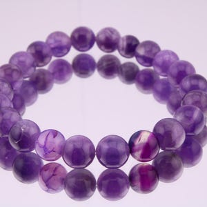 May include: A purple amethyst gemstone bracelet with round beads. The bracelet is made of natural stones and has a polished finish.
