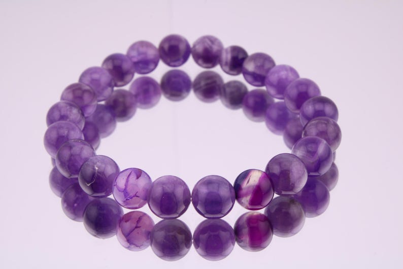May include: A purple amethyst gemstone bracelet with round beads. The bracelet is made of natural stones and has a polished finish.