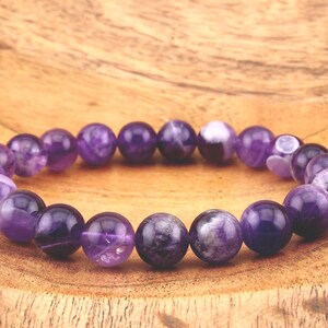 May include: A purple amethyst gemstone bracelet with round beads. The bracelet is on a wooden surface.