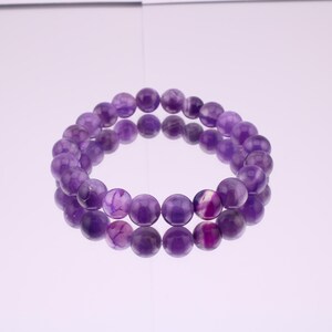 May include: A purple amethyst gemstone bracelet with round beads. The bracelet is made of natural stones and is a beautiful piece of jewelry.