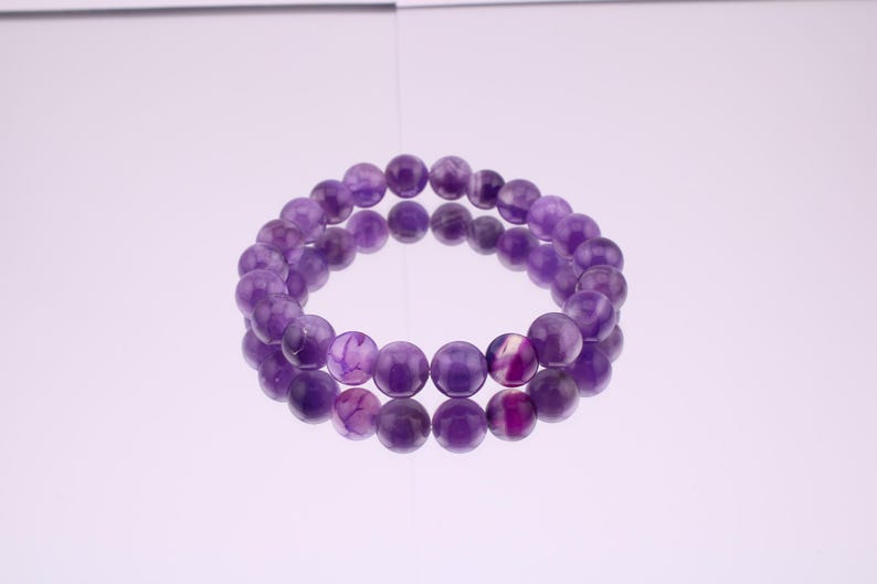 May include: A purple amethyst gemstone bracelet with round beads. The bracelet is made of natural stones and is a beautiful piece of jewelry.