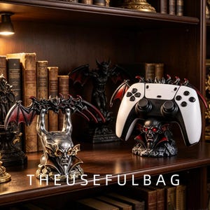 May include: Two gothic-style controller stands featuring sculpted demon heads with red eyes and bat wings. One stand is empty, while the other holds a white and black video game controller. The text THEUSEFULBAG is printed at the bottom of the image.