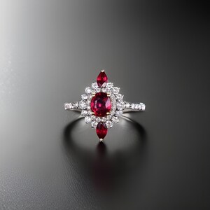 May include: A silver ring featuring a large red ruby surrounded by smaller diamonds. The ruby is set in a flower-shaped design with three smaller ruby accents.