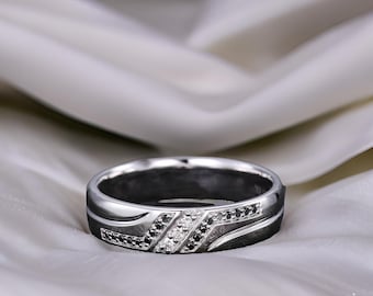 May include: A silver band with a black and white diamond design. The band has a textured surface and a curved shape.