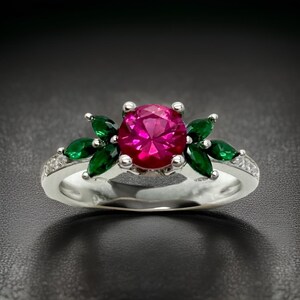 May include: A silver ring featuring a large, round, pink gemstone surrounded by smaller, green gemstones. The ring has a delicate band with small, clear gemstones.