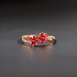 以下が含まれることがあります： 2つの赤いルビーの花のデザインが施された金の指輪。指輪には小さなダイヤモンドがセットされています。