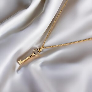 May include: A gold key pendant necklace with a delicate chain. The key has a simple design with a round keyhole and a straight shaft.