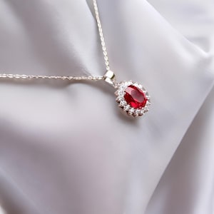 May include: A silver necklace with a red oval gemstone surrounded by smaller white gemstones.