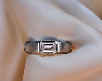 May include: A silver band ring with a clear emerald-cut diamond.