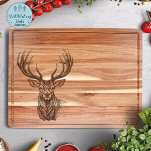 Könnte beinhalten: Ein Schneidebrett aus Holz mit einem lasergravierten Design eines Hirschkopfes. Das Brett hat eine natürliche Holzmaserung und eine hellbraune Farbe. Der Text "Prittlewood Craft Supplies" ist in der oberen linken Ecke des Bretts graviert.