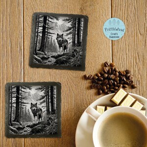 May include: Two black and white slate coasters with a wolf in a forest scene. The coasters are square and have a smooth, polished surface. The wolf is standing in the middle of the forest, looking out at the viewer. The forest is made up of tall trees and a stream running through it. The coasters are perfect for adding a touch of nature to your home decor.