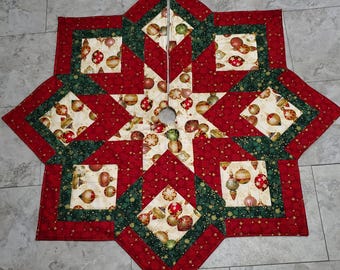 May include: A star-shaped Christmas tree skirt with a festive design. The skirt features a patchwork pattern of red, green, and cream-colored fabrics. The cream-colored fabric is printed with gold and red Christmas ornaments. The skirt has a hole in the center.