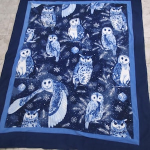 May include: A navy blue blanket featuring a repeating pattern of owls in shades of blue and white. The owls are depicted in various poses, set against a background of stylized branches and snowflakes. The blanket has a dark blue border.