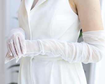May include: A pair of white elbow-length gloves made of sheer fabric. The gloves are gathered at the wrist and have a delicate, feminine look.