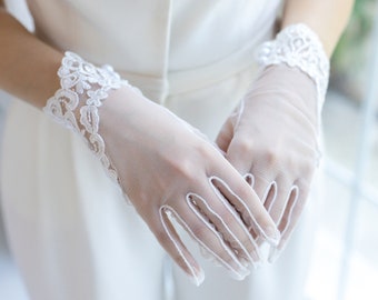 May include: A pair of white lace gloves with delicate floral embroidery. The gloves are made of sheer mesh fabric and have a fitted design.