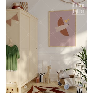 Könnte beinhalten: Ein weißer Holzschrank mit einem grünen Kleid, das an einem Kleiderbügel hängt. Ein gerahmtes Bild mit rosa Hintergrund und abstrakten Formen in Braun und Gelb hängt an der Wand. Ein Stoffgiraffen- und Elefantenspielzeug liegen auf dem Boden vor dem Schrank.