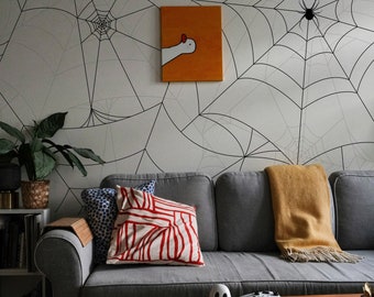 May include: A gray sofa with red and white striped pillows and a yellow throw blanket. The wall behind the sofa is decorated with a black and white spiderweb pattern wallpaper. A small ghost figurine sits on a wooden coffee table in front of the sofa.