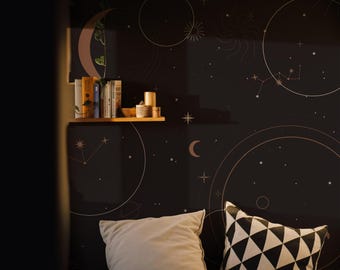 Puede incluir: Un papel tapiz celestial negro y dorado con una luna creciente, estrellas y planetas. El papel tapiz está en un dormitorio con una cama, almohadas y una estantería con libros y velas.