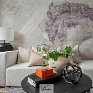 Può includere: Un salotto con un divano grigio chiaro e cuscini fantasia. Un tavolino rotondo nero espone libri, una scatola arancione, una sfera decorativa e un vaso con verde. Un grande murale di una scultura è sulla parete.