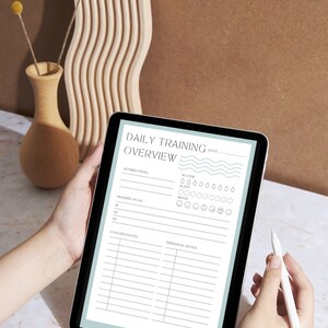 May include: A digital tablet displaying a daily training overview template with sections for affirmations, training plan, coaches notes, and personal notes. The template includes icons for water intake, sleep, and mood tracking.