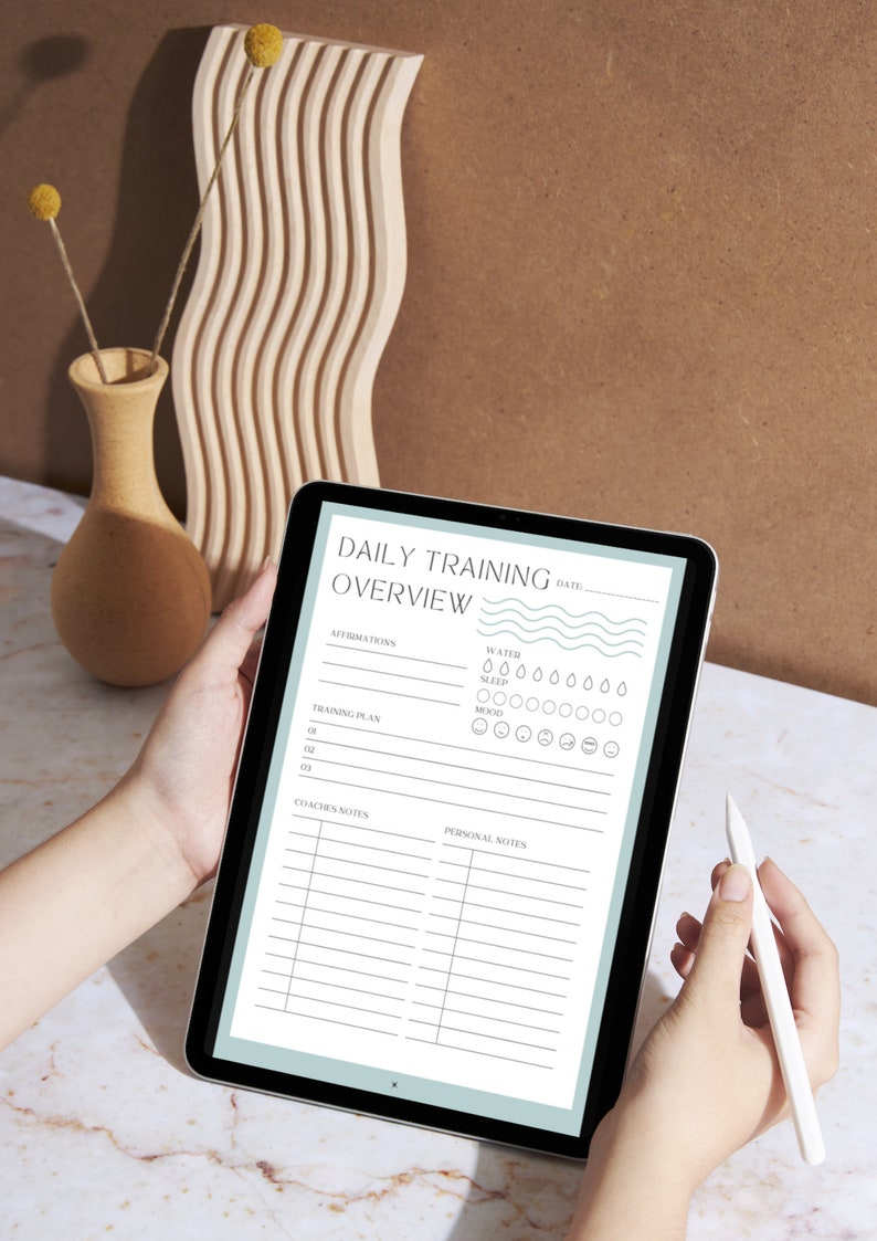 May include: A digital tablet displaying a daily training overview template with sections for affirmations, training plan, coaches notes, and personal notes. The template includes icons for water intake, sleep, and mood tracking.