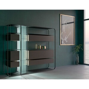 May include: A modern, open-plan bookshelf with glass shelves and a black metal frame. The bookshelf is illuminated with a soft, blue light. The bookshelf is in a room with a large window and a framed print on the wall.