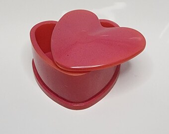 May include: A heart-shaped trinket box with a lid. The box and lid are a vibrant pink color.