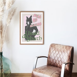 May include: A framed poster with a pink and green design. The poster features a woman wearing a hat and a black jacket. The text on the poster reads "Bean Up Heirarchy" and "Usaid Dogbuth".