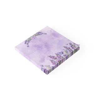 May include: Square notepad with a lavender floral design. The notepad features a watercolor-style background in shades of purple, with lavender sprigs and butterflies adorning the edges. The edges of the notepad are striped with purple and green.