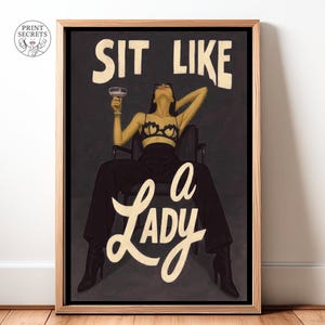 May include: Framed art print with the text "SIT LIKE a LADY" in a vintage style. The artwork depicts a person in a chair holding a cocktail. The person is wearing a bra and trousers. The background is dark.