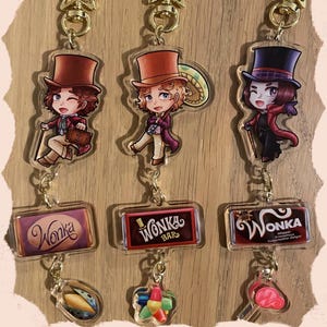 May include: Keyrings featuring characters from a fantasy story. The keyrings have gold-coloured star-shaped clasps. The top row shows three characters in top hats and coats. The bottom row shows Wonka Bar and candy-themed charms.