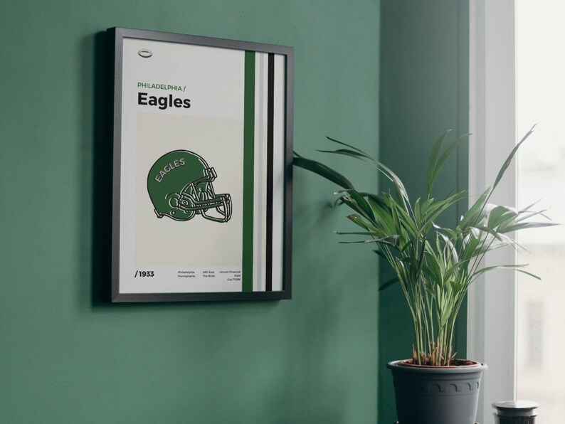 May include: A framed poster with a green and white striped background. The poster features a black and white illustration of a football helmet with the word "Eagles" on it. The text "Philadelphia/Eagles" and "1933" are also on the poster.
