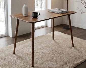 May include: A rectangular wooden desk with four tapered legs, featuring a smooth brown surface. On the desk sits a white diffuser, a dark ceramic mug on a coaster, and a book titled The Nordic Home. The desk is positioned in a room.