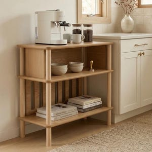 Peut inclure: Étagère de cuisine en bois clair à trois niveaux, avec une machine à expresso blanche, des bocaux de grains de café et des bols en céramique. L'étagère contient également des livres de cuisine et un tamper à café doré.
