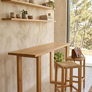 May include: A light wood bar table and two matching stools with woven seats. The table has a rectangular top and square legs. The stools are next to the table. Three wooden shelves are mounted on the wall, holding pottery and plants.