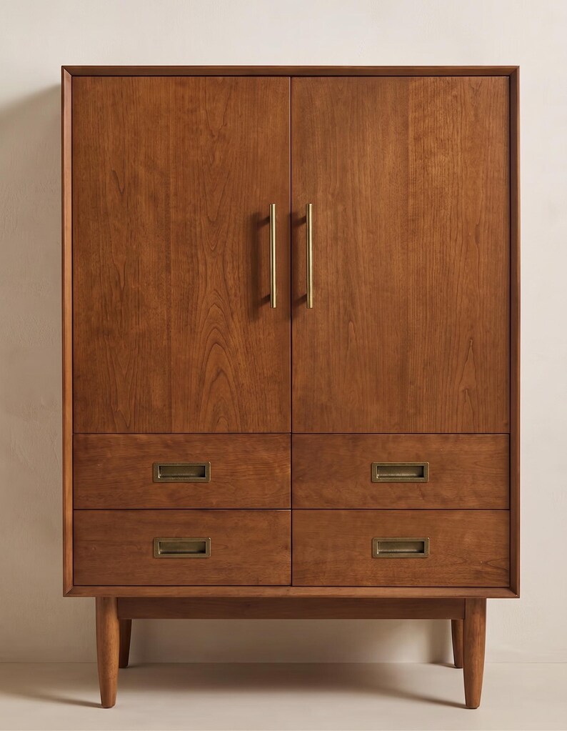 Op de afbeelding: Een houten kast in mid-century modern stijl, met twee deuren en vier laden. De kast is warmbruin met messingkleurige handgrepen en lade-trekkers. Hij staat op vier taps toelopende poten.