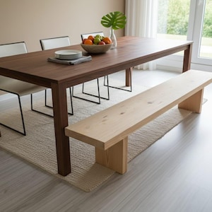 Könnte beinhalten: Ein modernes Esszimmer-Set mit einem dunkelbraunen rechteckigen Tisch, vier weißen Stühlen und einer hellen Holzbank. Eine Schale mit Obst und eine Vase mit einem grünen Blatt stehen auf dem Tisch. Der Tisch steht auf einem beigen Teppich.