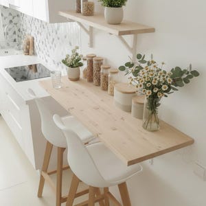 May include: A bright, modern kitchen with a light wood countertop and two white chairs. Shelves hold jars of food and a potted plant. A vase of flowers adds a touch of color to the minimalist design.