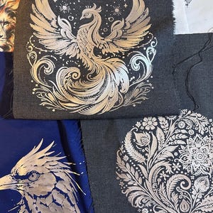 May include: Two pieces of fabric with silver metallic designs. One piece has a silver phoenix design on a dark grey background. The other piece has a silver floral design on a dark grey background.