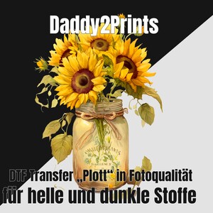 Könnte beinhalten: Ein Strauß gelber Sonnenblumen in einem durchsichtigen Glas mit einem braunen Band, das um den oberen Rand gebunden ist. Das Glas hat ein Etikett mit der Aufschrift "EMBLEMAMOS STARILENE S". Der Text "DTF Transfer, "Plott" in Fotoqualität für helle und dunkle Stoffe" befindet sich am unteren Rand des Bildes.
