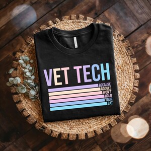 Può includere: T-shirt nero con la scritta "VET TECH" in colori pastello sopra strisce orizzontali. Il testo "BECAUSE GOOGLE WON'T HOLD YOUR CAT" è stampato sotto. La maglietta è esposta su un tappetino intrecciato.