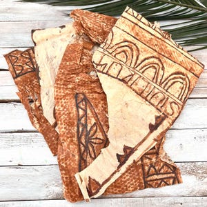 Könnte beinhalten: Mehrere Stücke handgefertigtes, strukturiertes Papier in Braun- und Cremetönen. Das Papier weist dunkelbraune geometrische und florale Muster auf. Die Stücke sind auf einer weißen Holzoberfläche mit einem grünen Blatt im Hintergrund angeordnet.