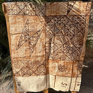 Op de afbeelding: Een rechthoekig stuk gebroken wit schorsdoek met donkerbruine, handgeschilderde geometrische patronen, waaronder vierkanten, driehoeken en een grote bliksemvorm. De onderrand toont de handgeschreven cijfers 14, 15 en 16.