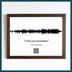 May include: A framed print with a white background features a black soundwave design. The text "I love you Grandma!" is displayed below the soundwave, followed by "Love, Rachel" and a QR code. The frame is a dark brown color.