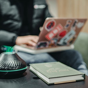 May include: A black and green essential oil diffuser with a book titled "Browse Both" on a dark wooden table.
