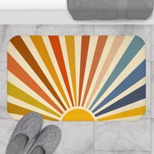 May include: A colorful bath mat with a retro sunburst design. The mat features a yellow sun with orange, red, brown, yellow, blue, and light blue rays.