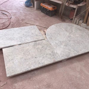 May include: Three light gray stone slabs of varying shapes. One is rectangular, another is a smaller rectangle, and the third is a rounded shape. The slabs have a mottled appearance and are likely for construction or design purposes.