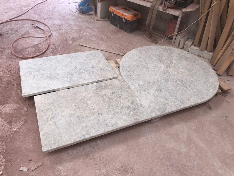 May include: Three light gray stone slabs of varying shapes. One is rectangular, another is a smaller rectangle, and the third is a rounded shape. The slabs have a mottled appearance and are likely for construction or design purposes.
